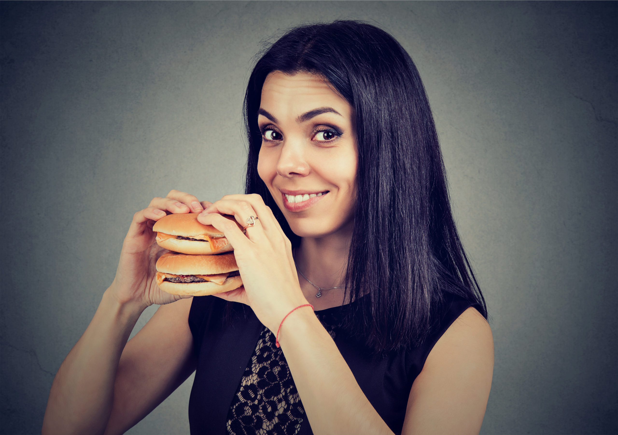 Lady in white t shirt trying to eat a burger with her mouth wide open