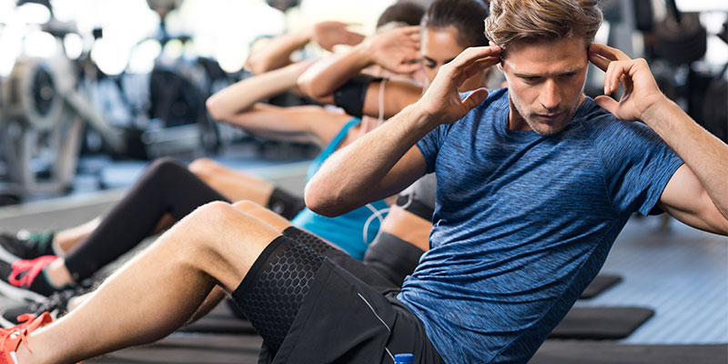 A young male athlete doing crunches at the gym with other people in the background